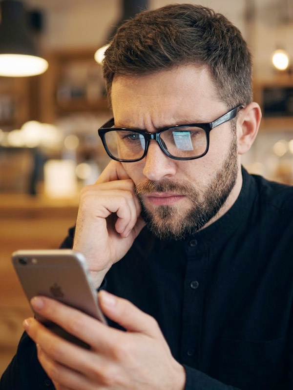 Homem mais velho de óculos pensando enquanto olha para o smartphone